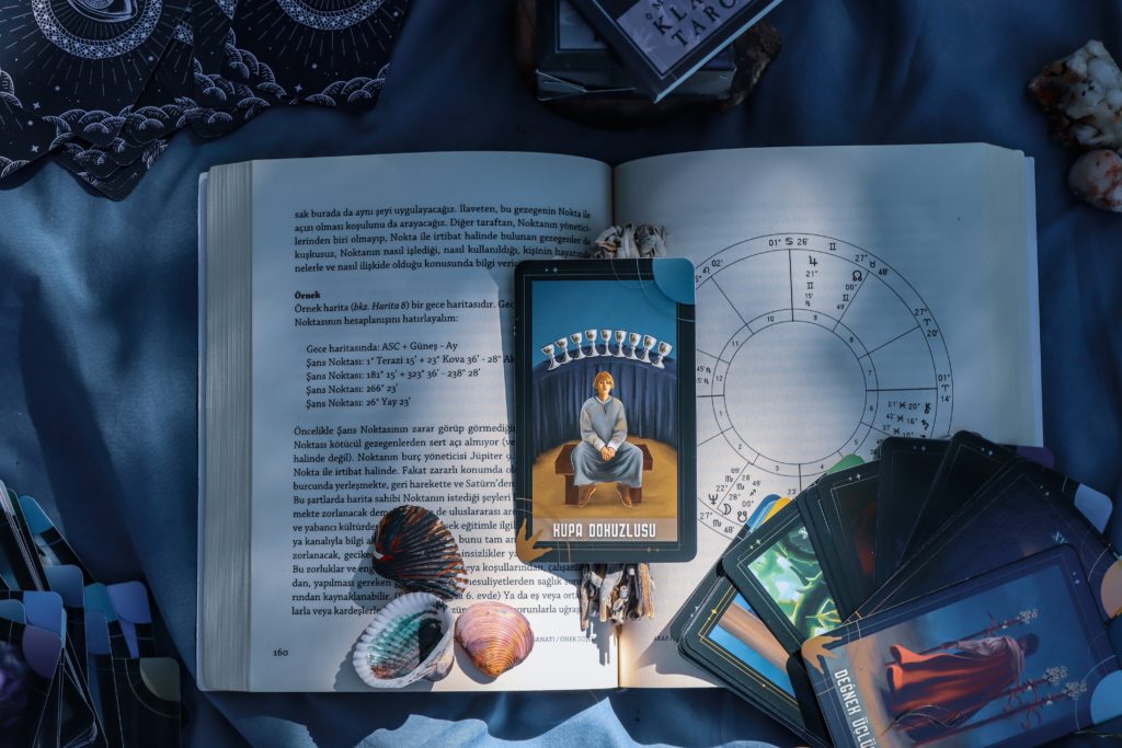 Tarot cards, shells, and stones on an open energy healing book. Photo by dilara irem
